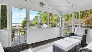 A covered porch with wicker furniture, large windows, and a view of a residential area. - Saratoga Lake, 3 Cottages + Private Beach With Dock (Saratoga Springs)