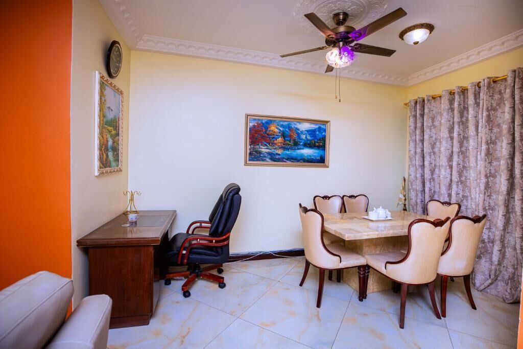 A room with a dining table, chairs, a desk, a chair, a ceiling fan, and a painting on the wall.