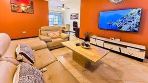 Ein Wohnzimmer mit einer Couch, einem Couchtisch, einem Fernseher und einer Uhr an der Wand.