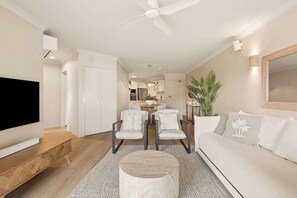 A modern living room with a TV, sofa, chairs, a round coffee table, and a ceiling fan. - Azure by Khove - Palm Beach (Palm Beach)