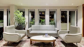 Un salón moderno con un sofá blanco, dos sillones, una mesa de centro y un ventanal con vistas a plantas de interior.