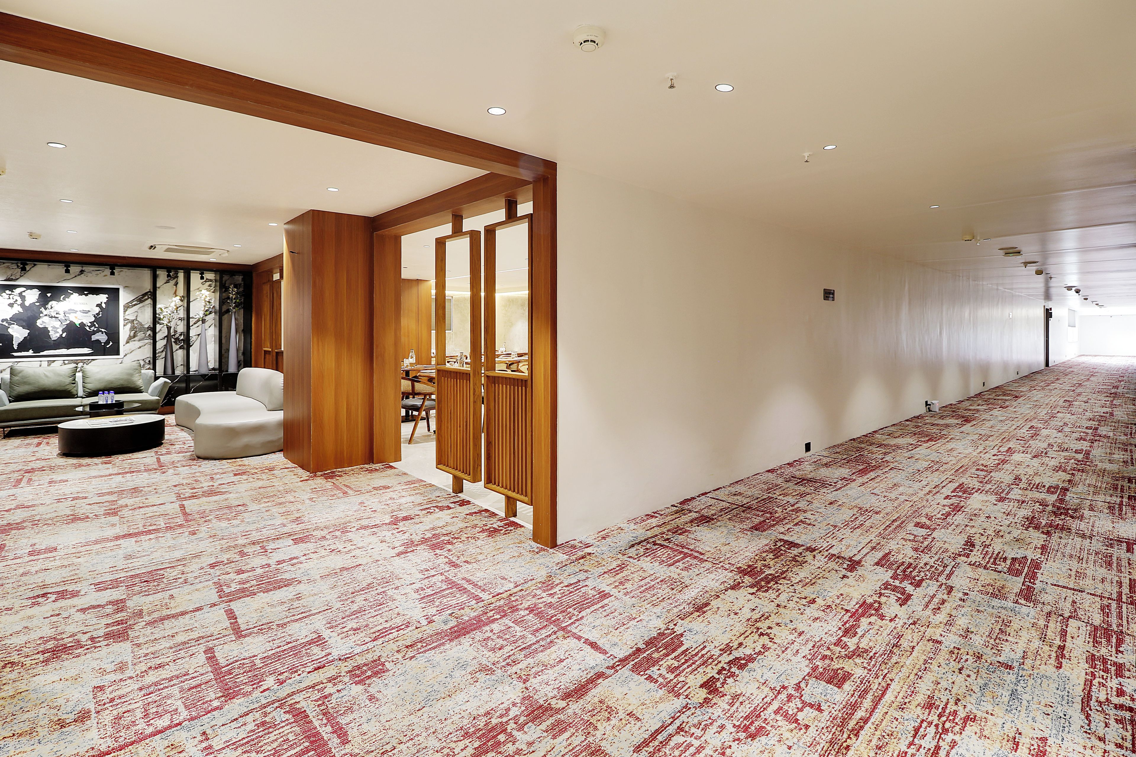 A hotel lobby with a large carpeted area, a seating area with a sofa and armchairs, and a wall-mounted world map.