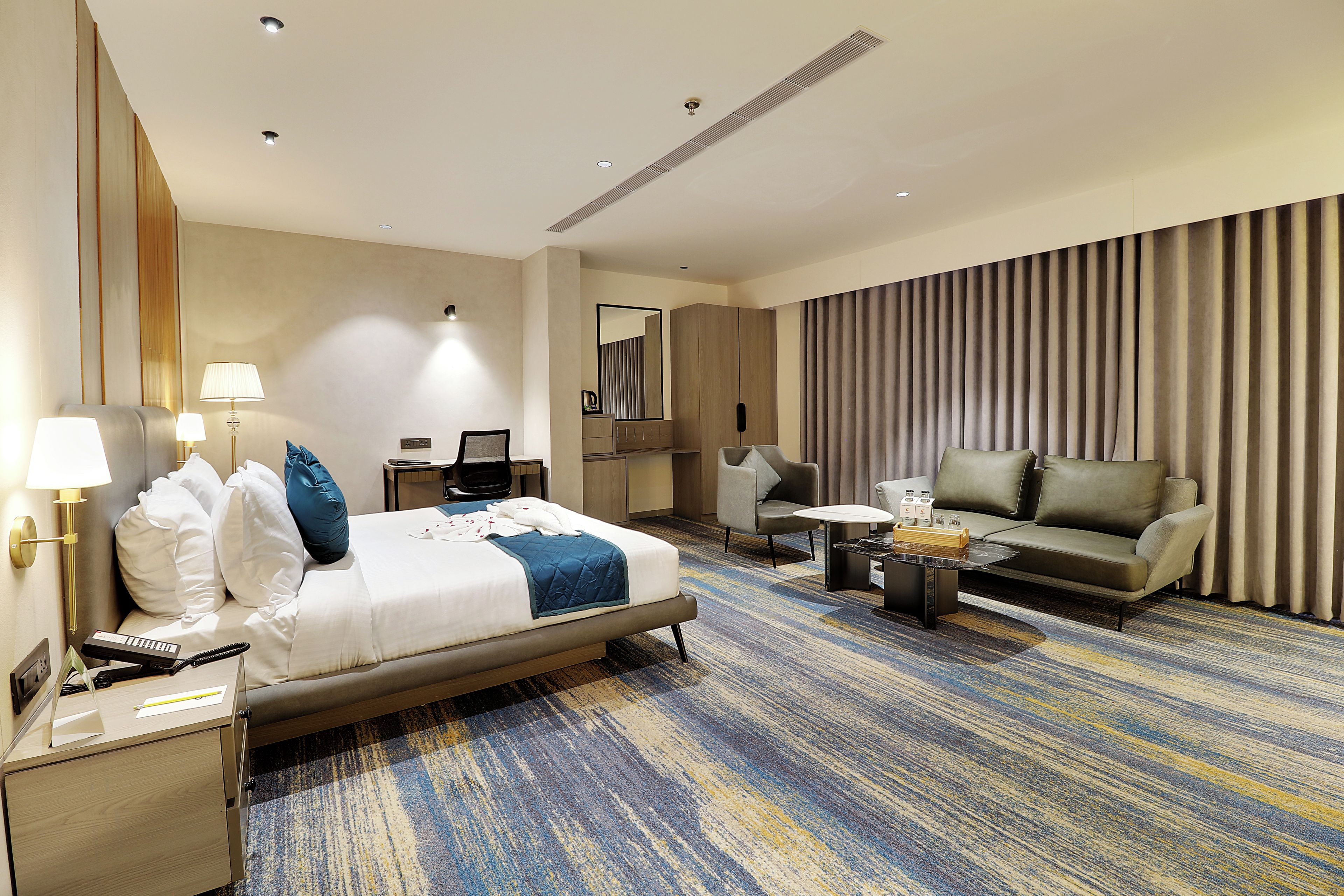 A hotel room with a bed, a desk, a sofa, a coffee table, and a large window with curtains.