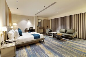 A hotel room with a bed, a desk, a sofa, a coffee table, and a large window with curtains. - Comfort INN Empire Morbi (Morbi)