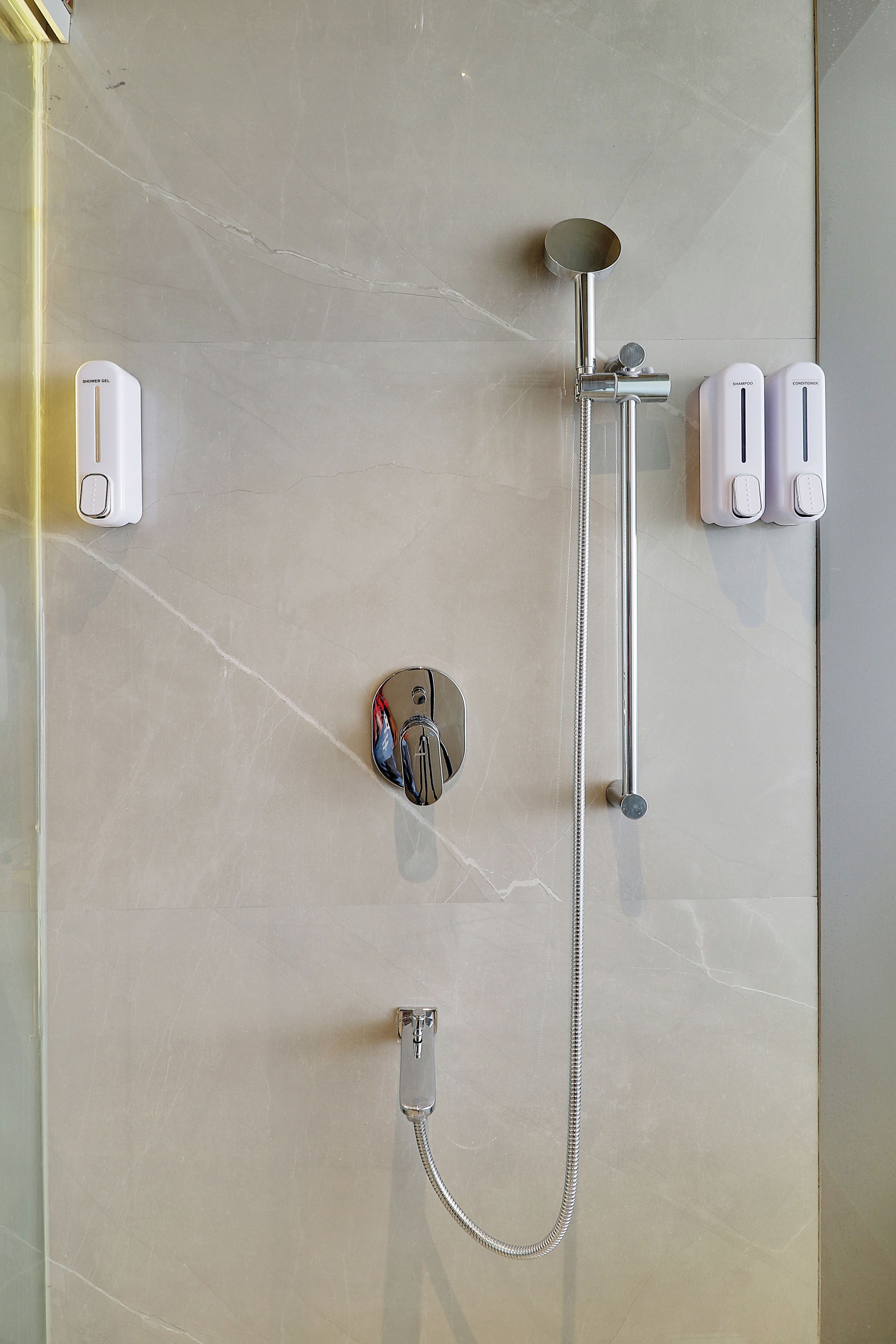 A bathroom with a shower, a handheld showerhead, a handheld shower attachment, and two wall-mounted soap dispensers.