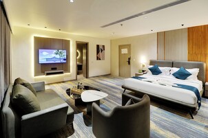 Habitación de hotel con cama, televisor, escritorio y zona de estar.