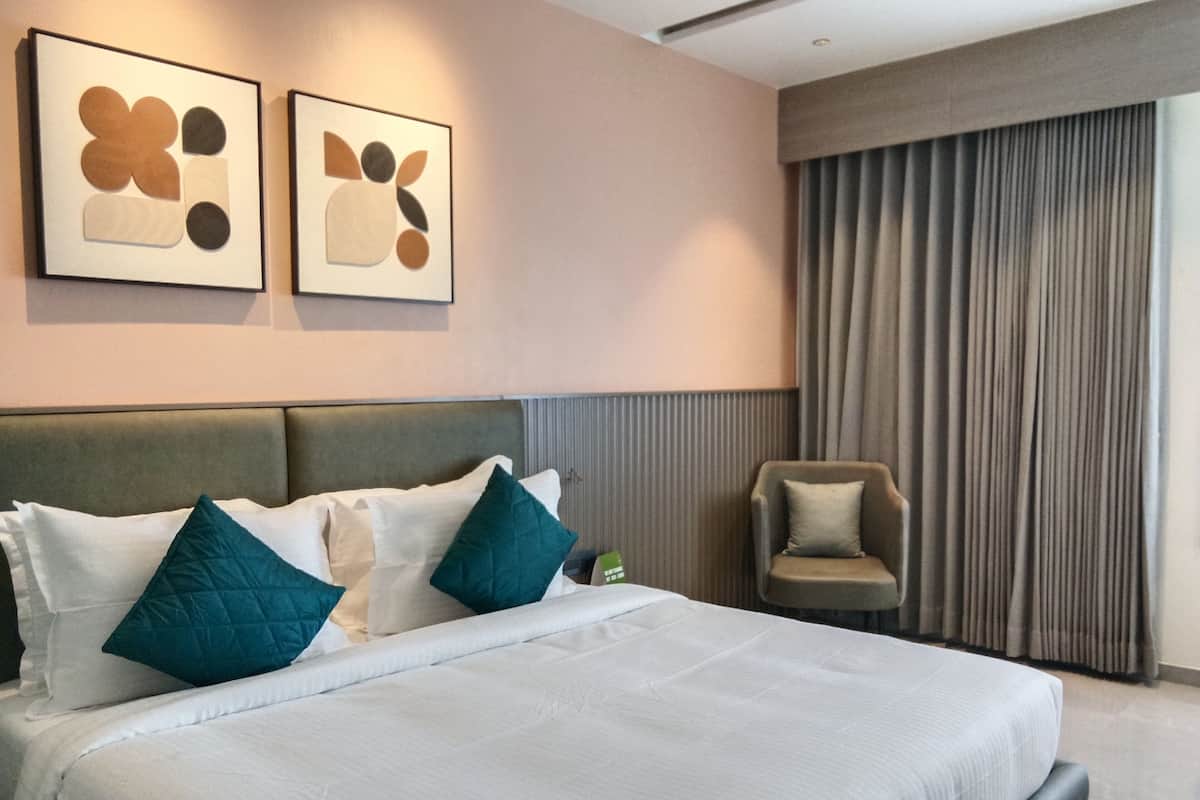 Ein modernes Hotelzimmer mit einem großen Bett, einer Kopfteil, einem Sessel und zwei abstrakten Bildern an der Wand.
