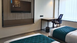 Habitació d'hotel amb dos llits, un escriptori, una cadira, televisió penjada a la paret i una finestra amb persianes.