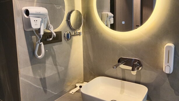 A bathroom with a hairdryer, a mirror, a sink, and a wall-mounted phone.