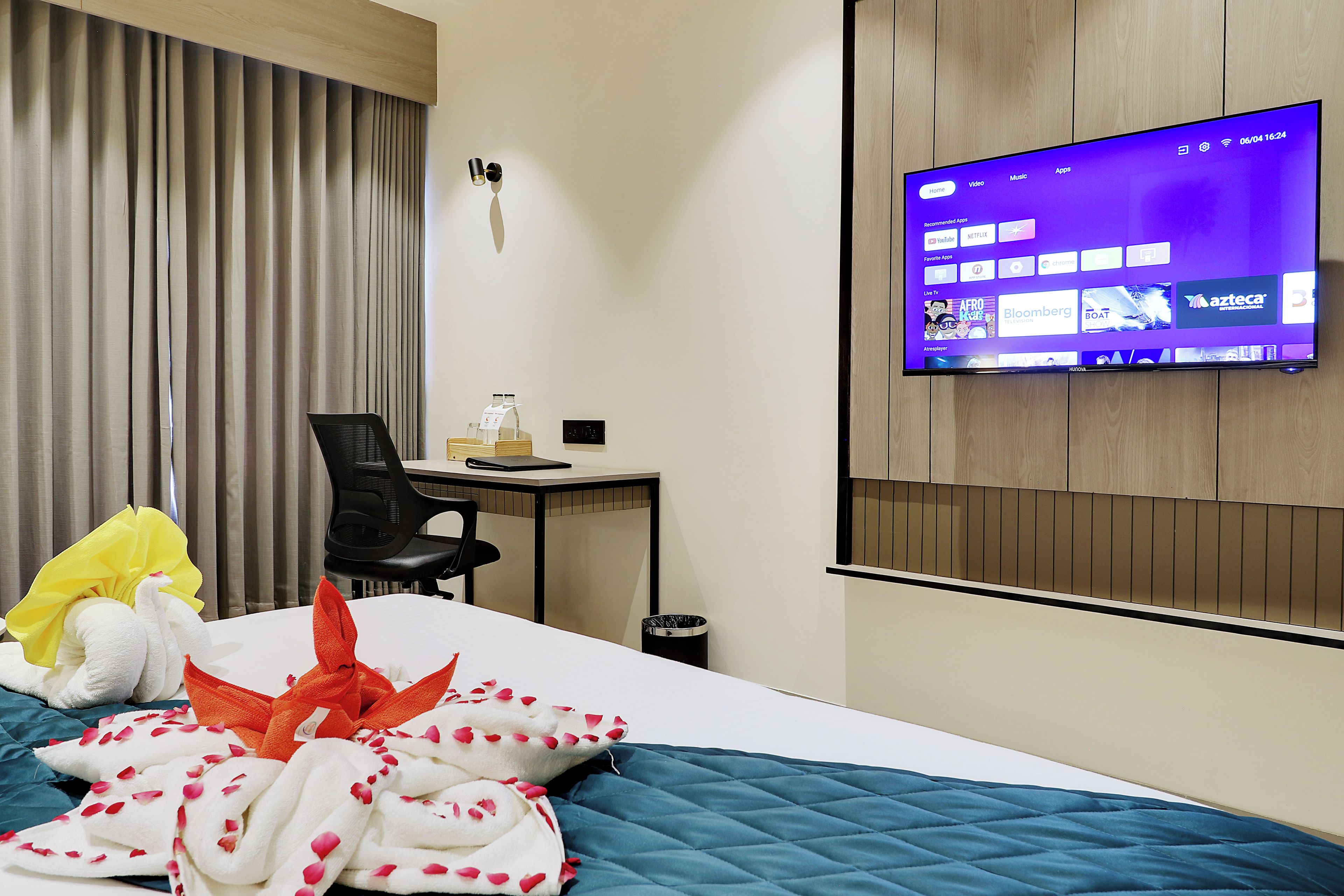 Habitación de hotel con cama, escritorio, silla, televisor montado en la pared y ventana con cortinas.