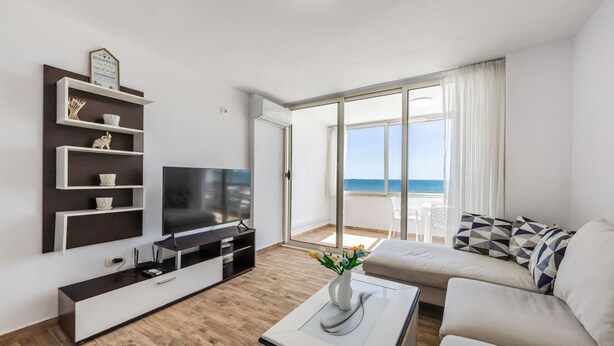 Un salon moderne doté d’un téléviseur à écran plat, d’un canapé, d  ’une table basse et d’un balcon offrant une vue sur la mer.