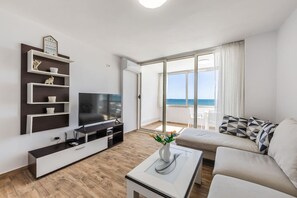 A modern living room with a flat-screen TV, a sofa, a coffee table, and a balcony with a view of the sea. - Aqua Vista Apartment Waterfront Balcony Escape (Durrës)