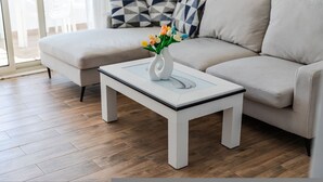 Un salon moderne avec un canapé blanc, une table basse blanche ornée d’un vase de fleurs et des coussins aux motifs géométriques.