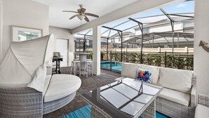 Eine sonnige Terrasse mit Glasveranda, Korbmöbeln, einem Pool und einem Deckenventilator.