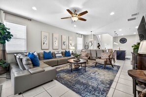 A modern living room with a sectional sofa, a coffee table, and a ceiling fan. - Windsor at Westside Resort • FREE RESORT • Sleeps 12 • Near Disney • Pool/Spa (Kissimmee)