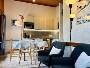Ein zeitgemäßer Essbereich mit einem Tisch für vier Personen, Holzkstühlen, einer Couch und einer Küche im Hintergrund.