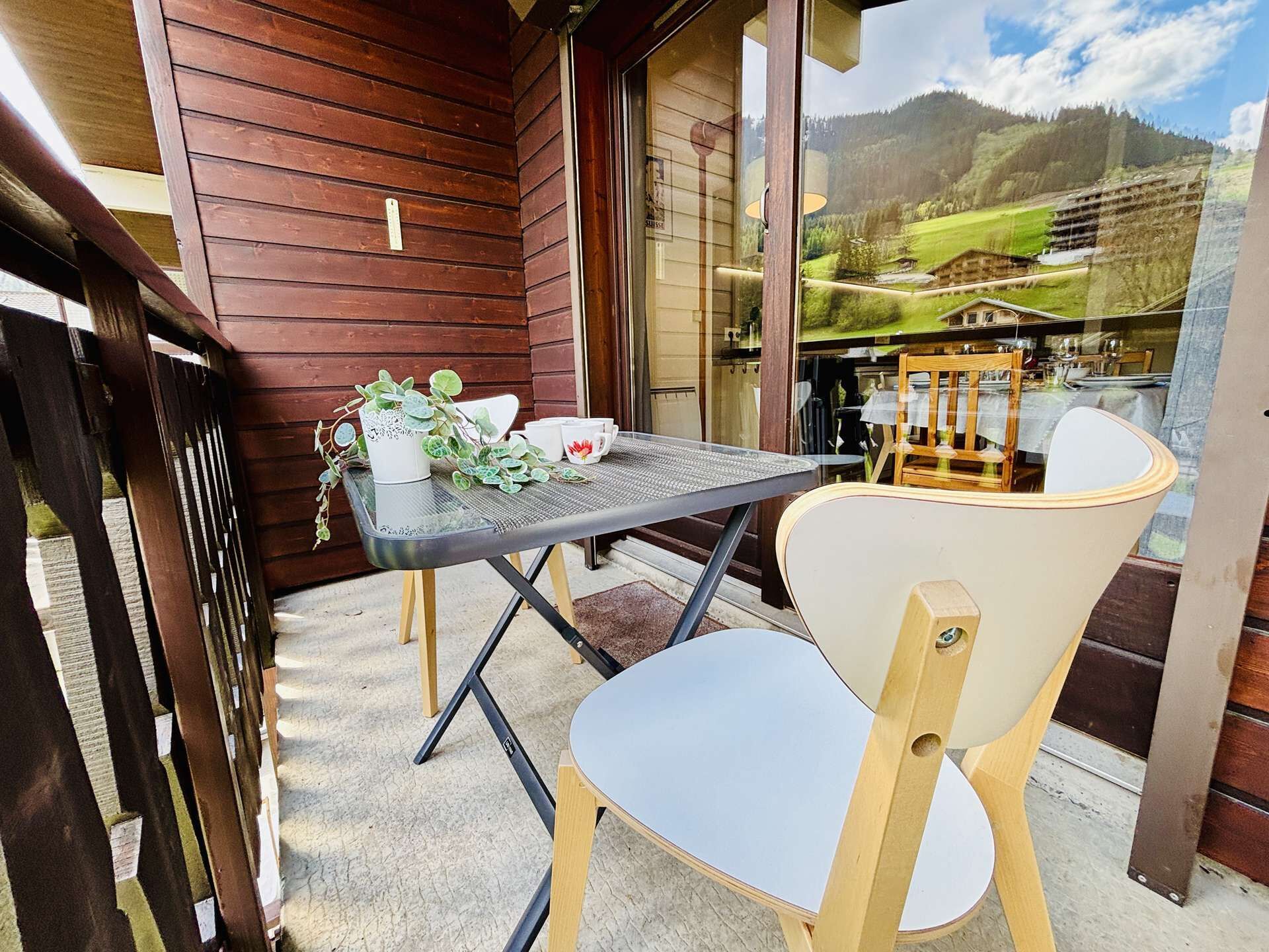 A balcony with a table and chairs, a potted plant, and a view of a mountain landscape.