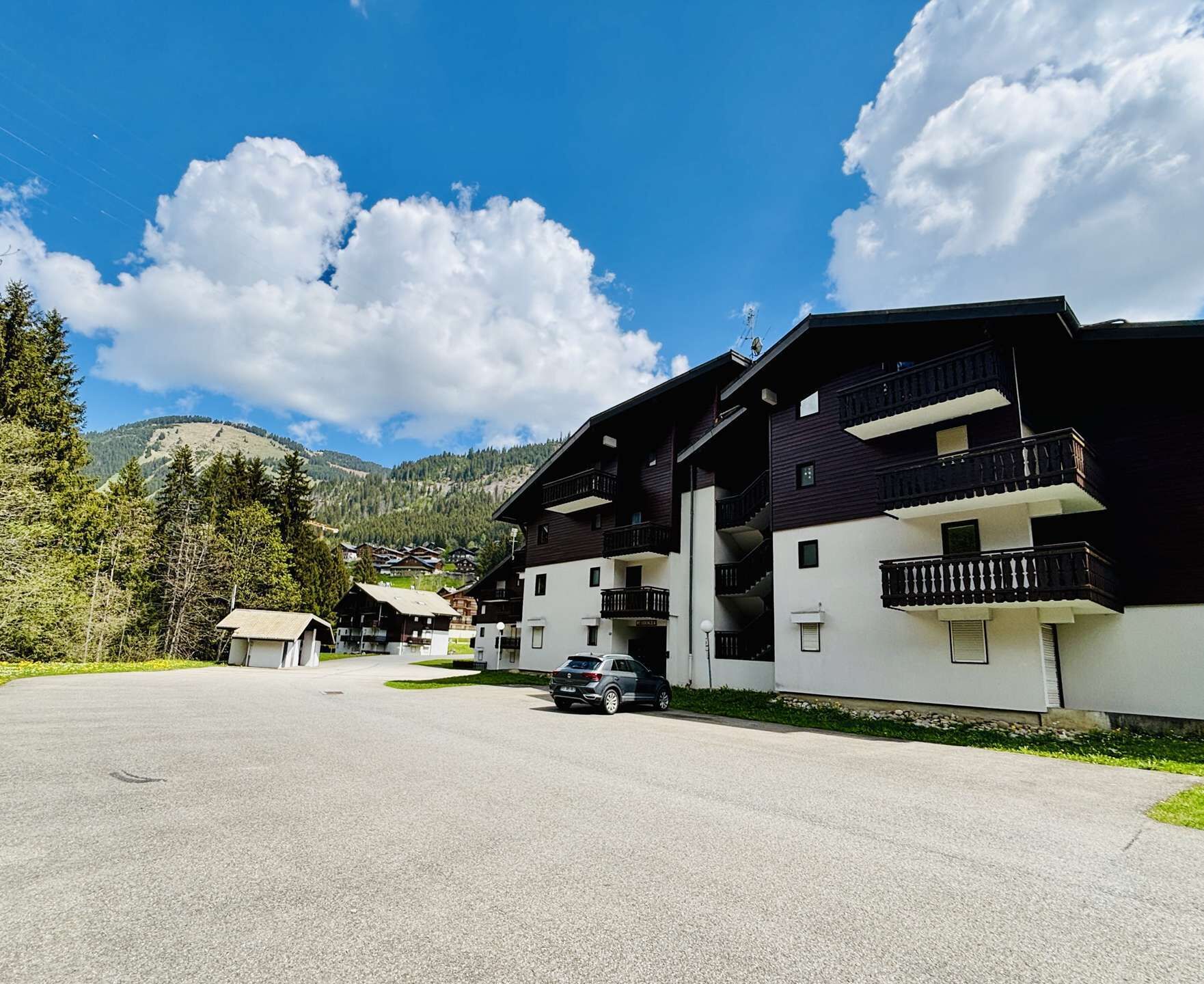 En bygning med flere etager, balkoner, parkeringsplads og et bjergrigt landskab i baggrunden.