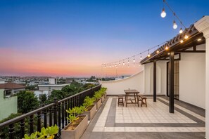 Eine Dachterrasse mit Blick auf die Stadt, einem Tisch, Stühlen und Lichterketten.