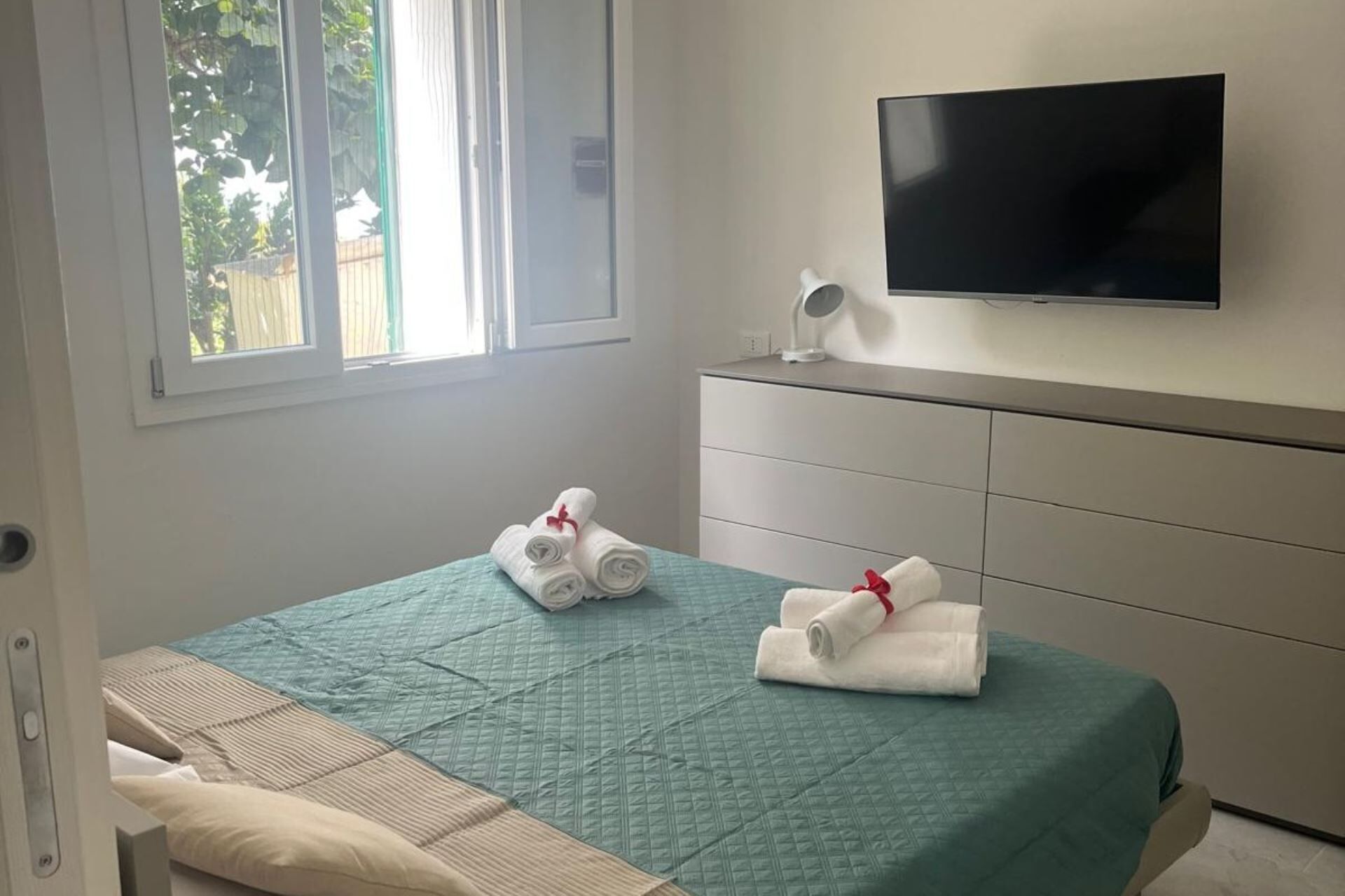 Ein Hotelzimmer mit Bett, Wandfernseher und Fenster mit Blick auf Grünflächen.