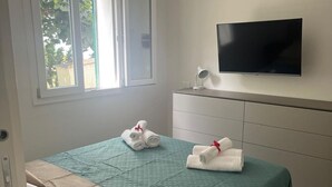 Camera d'albergo con un letto, una TV a muro e una finestra che si affaccia sul verde.
