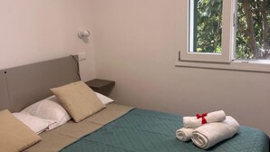 Un letto rifatto con cuscini, un comodino e una finestra con vista sugli alberi.