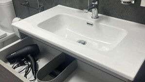 Un bagno con un lavandino bianco, uno specchio e un portasciugamani.