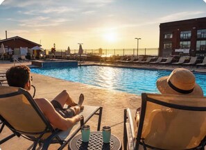 A poolside area with lounge chairs, a pool, and a sunset in the background. - Downtown Waterfront Stunning Views of Cedar Point! (Sandusky)