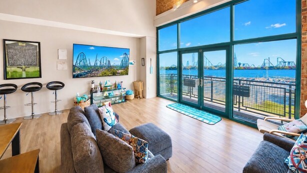 A spacious living area with a large window overlooking a body of water and a bridge, a sofa set, and a bar area with stools.