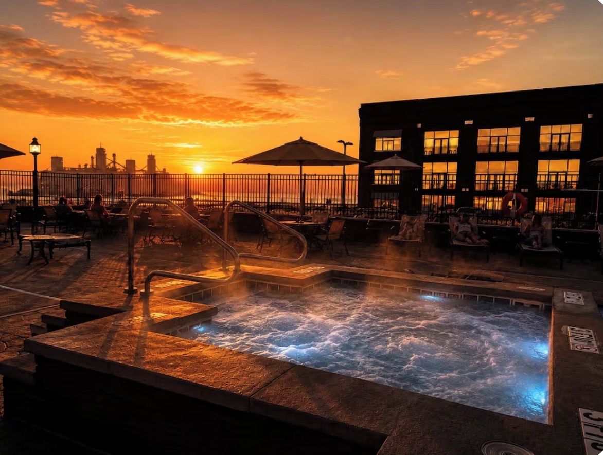A rooftop pool with a view of the sunset and city skyline.