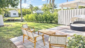 Eine Terrasse mit Korbmöbeln, einer Pergola und Blick auf ein Haus und Palmen.