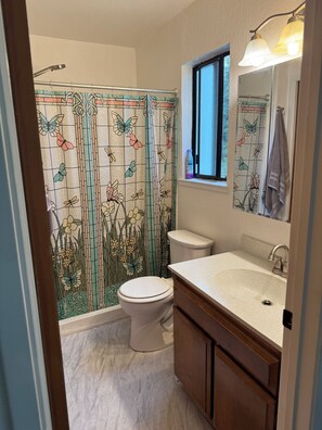 Een badkamer met toilet, wastafel en douchegordijn met bloem- en vlindermotieven.