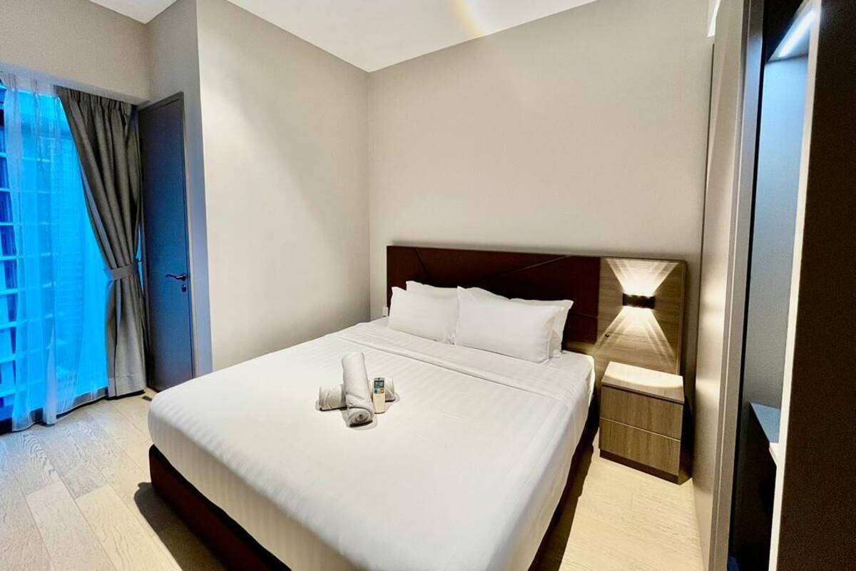 Habitación de hotel con una cama grande, una mesita de noche, una lámpara y vistas al exterior.