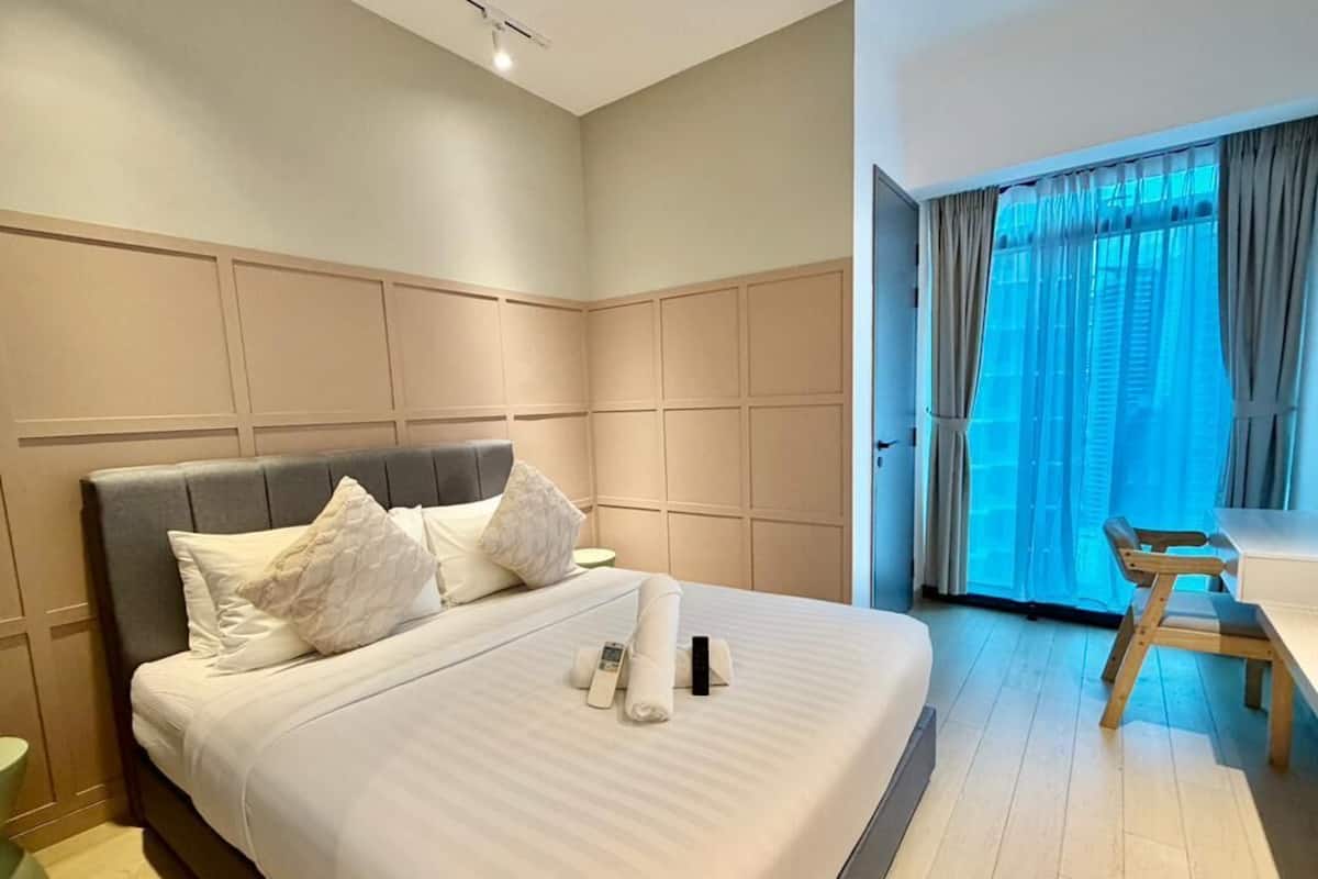 Habitación de hotel moderna con una cama grande, un banco de madera y vistas al exterior a través de un amplio ventanal.