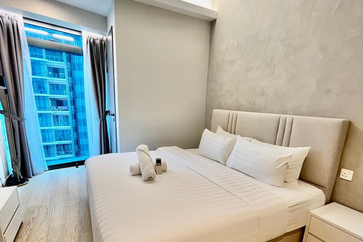 Una habitación de hotel moderna con una cama grande, un ventilador de techo, una mesita de noche y vista a un edificio por la ventana.