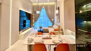 A modern dining area with a large table set for four, a sofa, and a view of a cityscape through large windows.