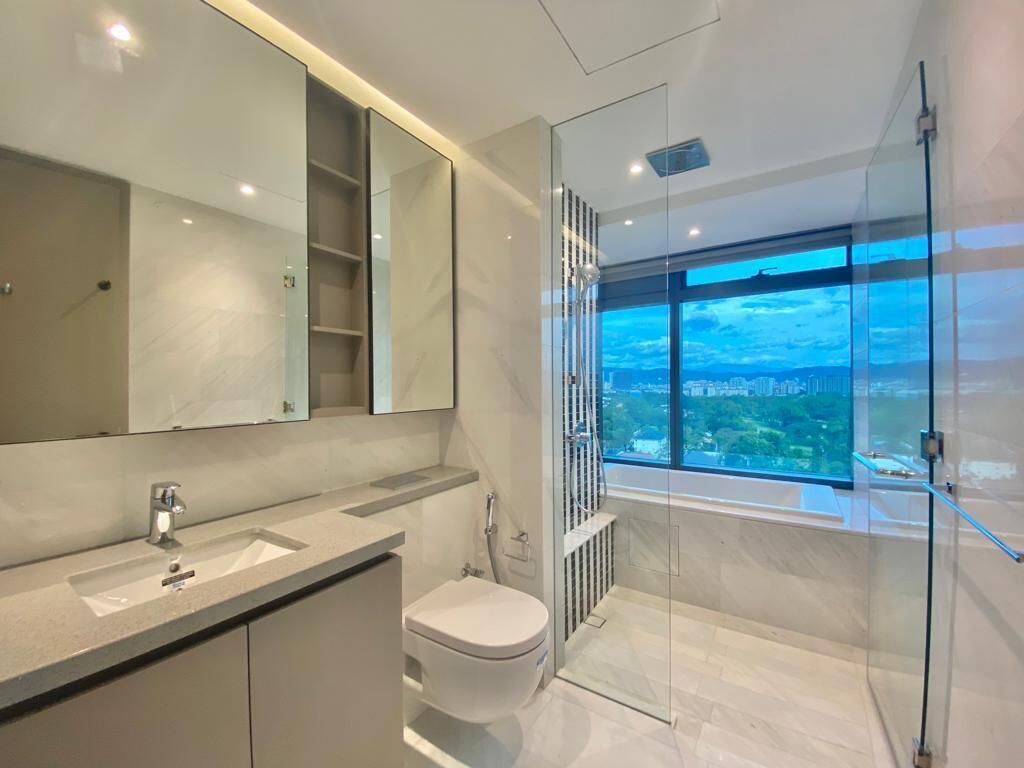 Un baño moderno con un espejo grande, un inodoro, cabina de ducha y vistas a un paisaje urbano a través de un ventanal.