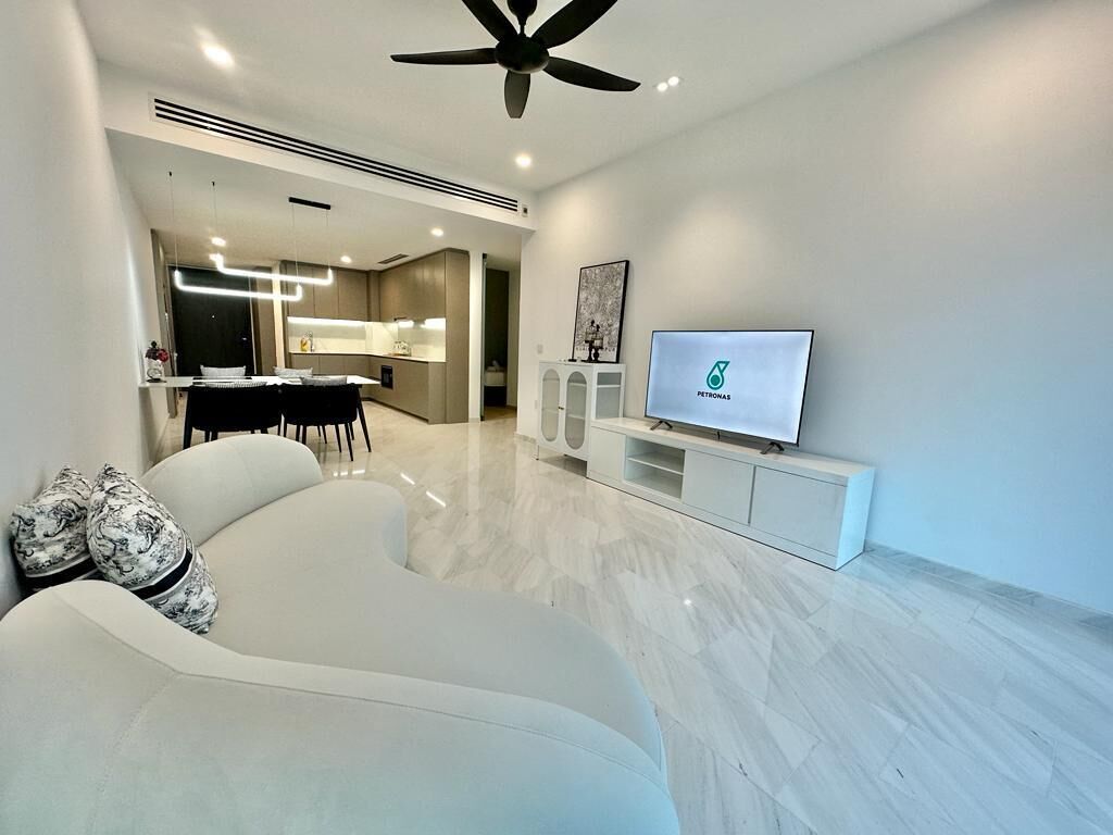 A modern living room with a sofa, a flat-screen TV, and a dining area in the background.