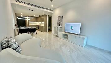 A modern living room with a sofa, a flat-screen TV, and a dining area in the background.