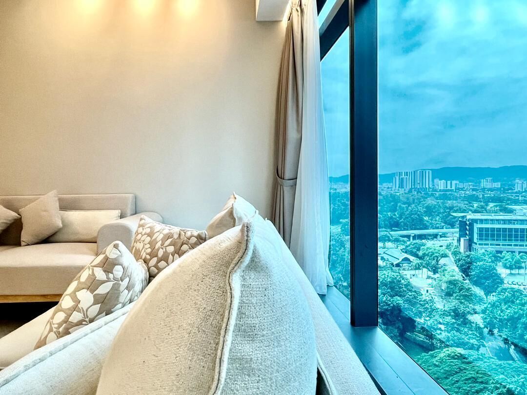 A modern room with a sofa, pillows, and a large window overlooking a cityscape.