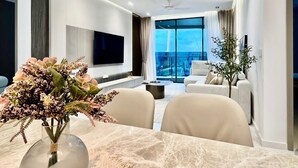 A modern living room with a flat-screen TV, a dining table with a vase of flowers, and a sofa.