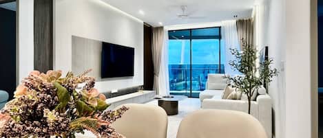 A modern living room with a flat-screen TV, a dining table with a vase of flowers, and a sofa.