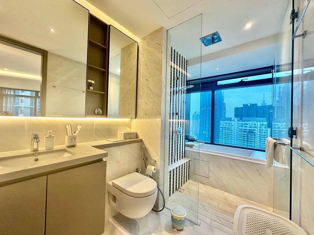 A modern bathroom with a toilet, sink, and shower area, featuring a large window with a city view.