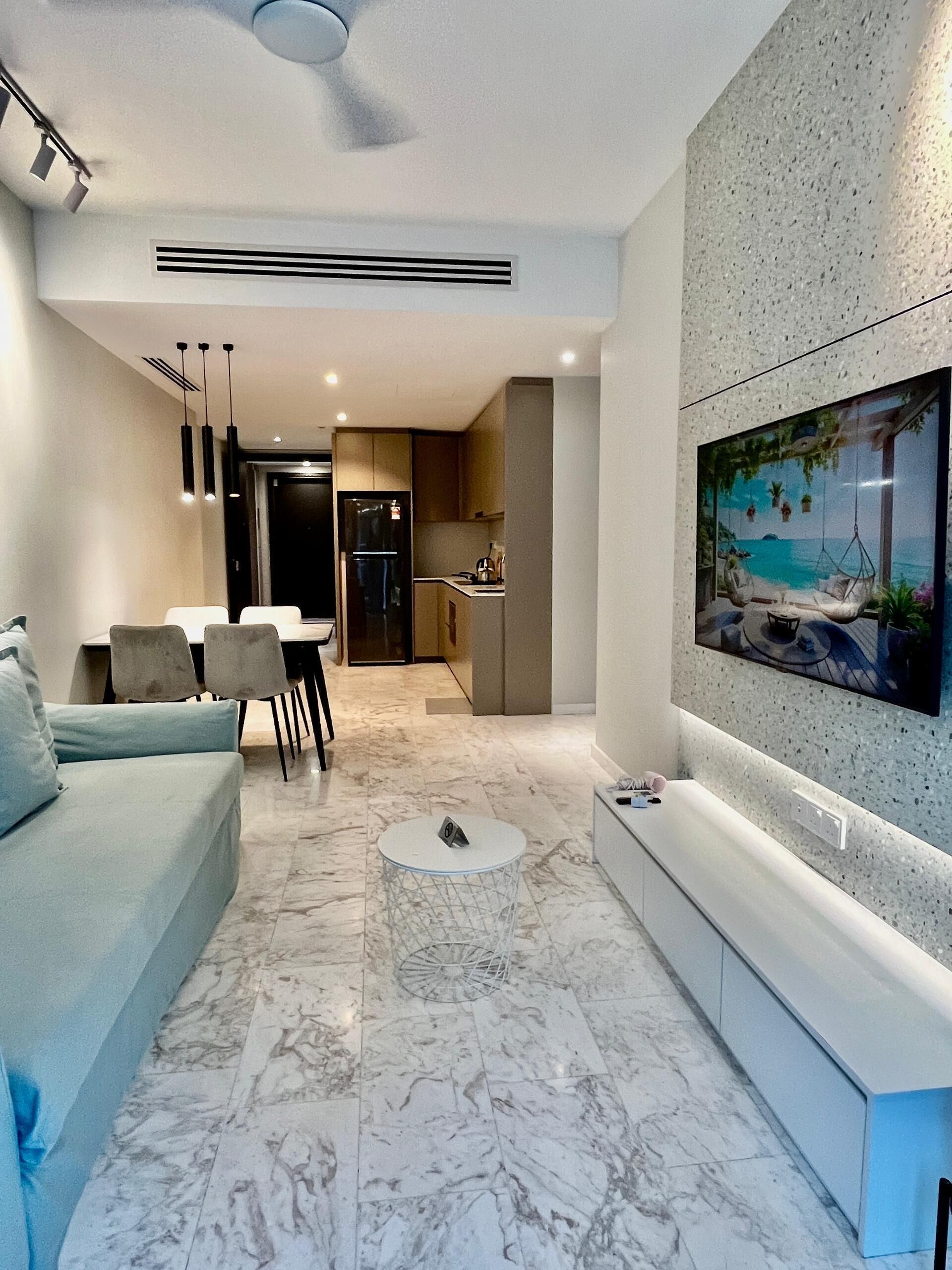 A modern living room with a sofa, dining table, chairs, a coffee table, and a TV mounted on a textured wall.