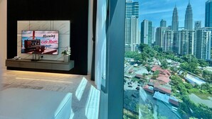 A modern interior with a TV displaying 'Morning Cafe Music,' a cityscape view, and a window overlooking a parking area.
