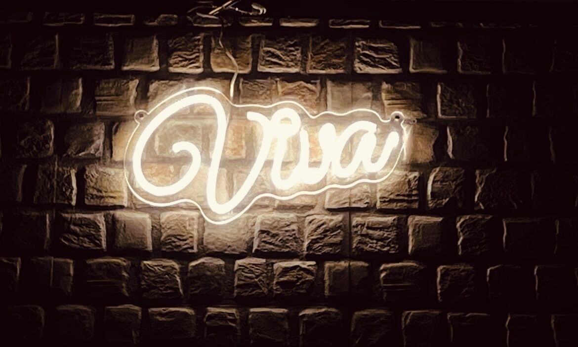 Eine Neonreklame mit der Aufschrift 'Via' an einer Ziegelwand.