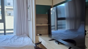 Een hotelkamer met een bed, een bureau met een flatscreen-tv, een stoel en een raam met gordijnen.