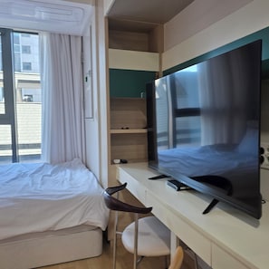 Ein Hotelzimmer mit Bett, Schreibtisch, Flachbildfernseher, Stuhl und einem fenster mit Vorhängen.