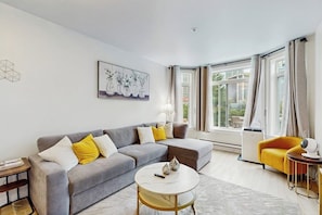 Ein modernes Wohnzimmer mit einem grauen Sofa, gelben Kissen, einem runden Couchtisch und einem gelben Sessel.