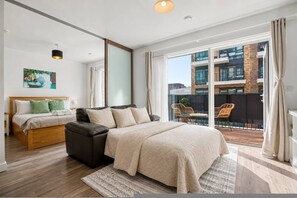 Een slaapkamer met een groot bed, een kleiner bed, een slaapbank en een balkon met uitzicht op gebouwen.